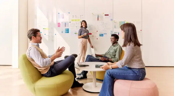 Team discute idee davanti a lavagna con grafici. Eni assume 50 diplomati e laureati, offrendo opportunità di crescita.