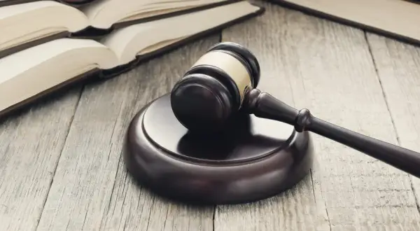 Martelletto da giudice su tavola di legno, con libri aperti sullo sfondo. Simbolo di giustizia e di studi di scienze giuridiche Pegaso.