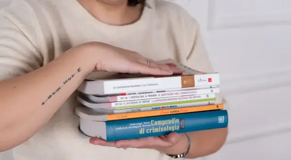 Mani che sorreggono libri, tra cui un "Compendio di criminologia". Quanti anni sono passati da quando si è iniziato a studiare il crimine?