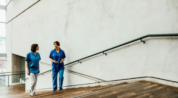 Due fisioterapiste in camice blu discutono sulle scale, forse valutando nuove offerte lavoro fisioterapista.