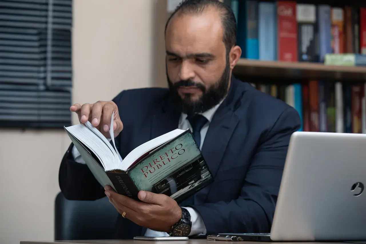 Uomo barbuto in giacca e cravatta legge un libro di diritto pubblico, forse cercando consigli su che liceo fare per diventare avvocato.