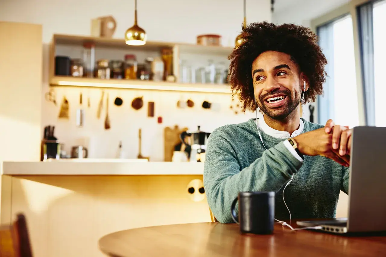 Uomo sorridente con cuffie lavora da casa al suo laptop, godendosi la flessibilità dei **work from home jobs**.