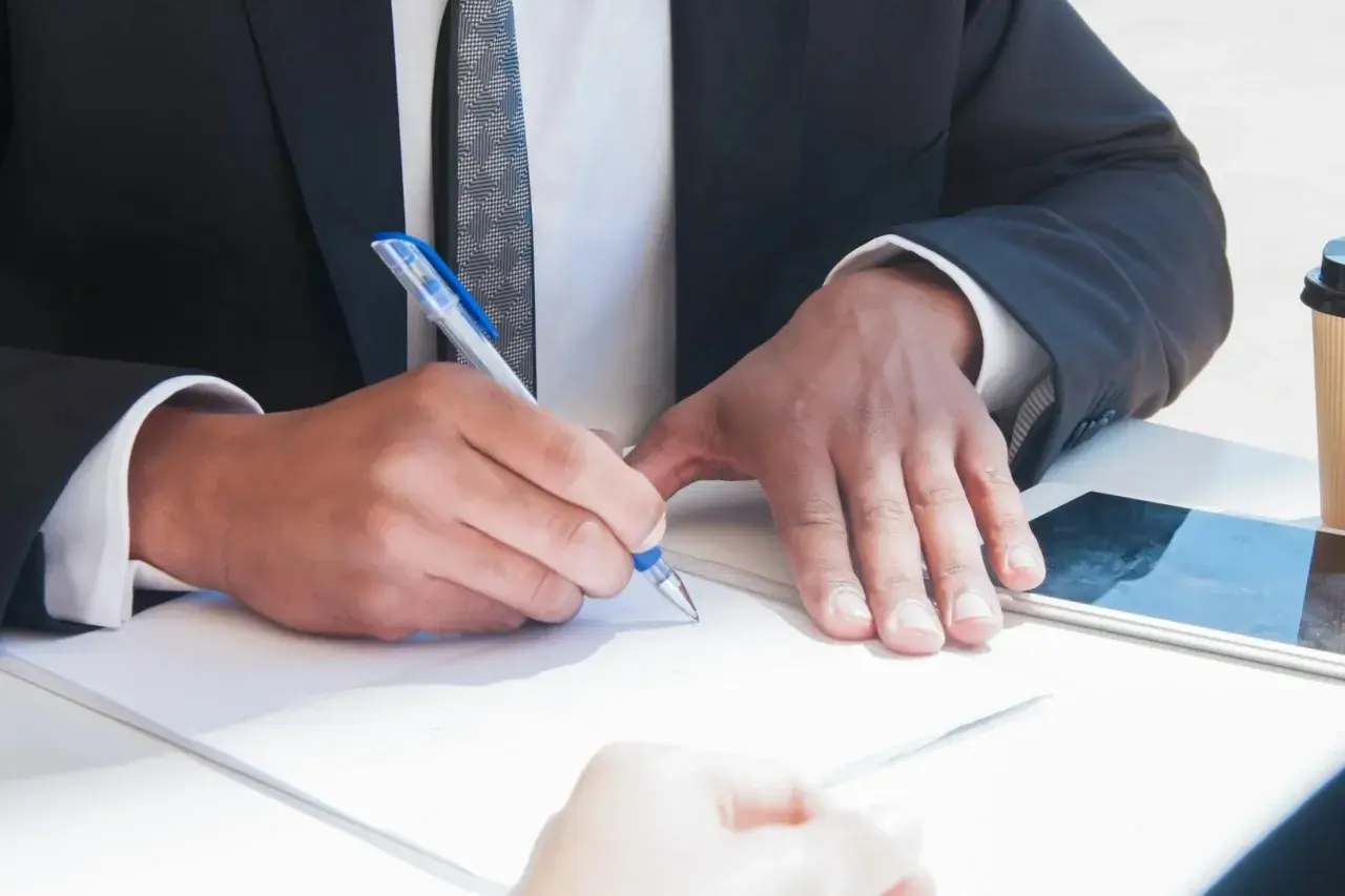 Un uomo in giacca e cravatta firma un documento, mostrando cosa fa un notaio: autentica e garantisce accordi legali con professionalità.