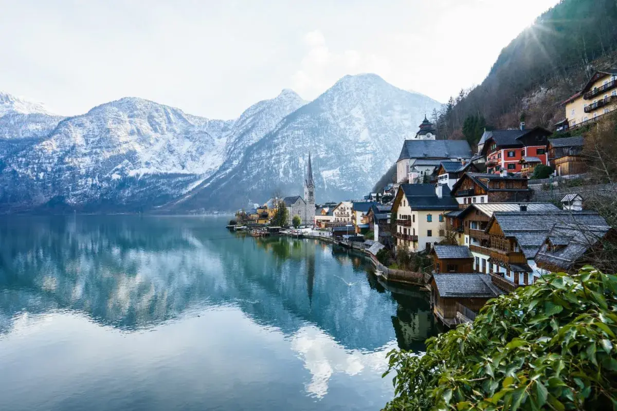 Villaggio alpino con case in legno sul lago, montagne innevate sullo sfondo. Ideale per offerte di lavoro stagione invernale vitto e alloggio.
