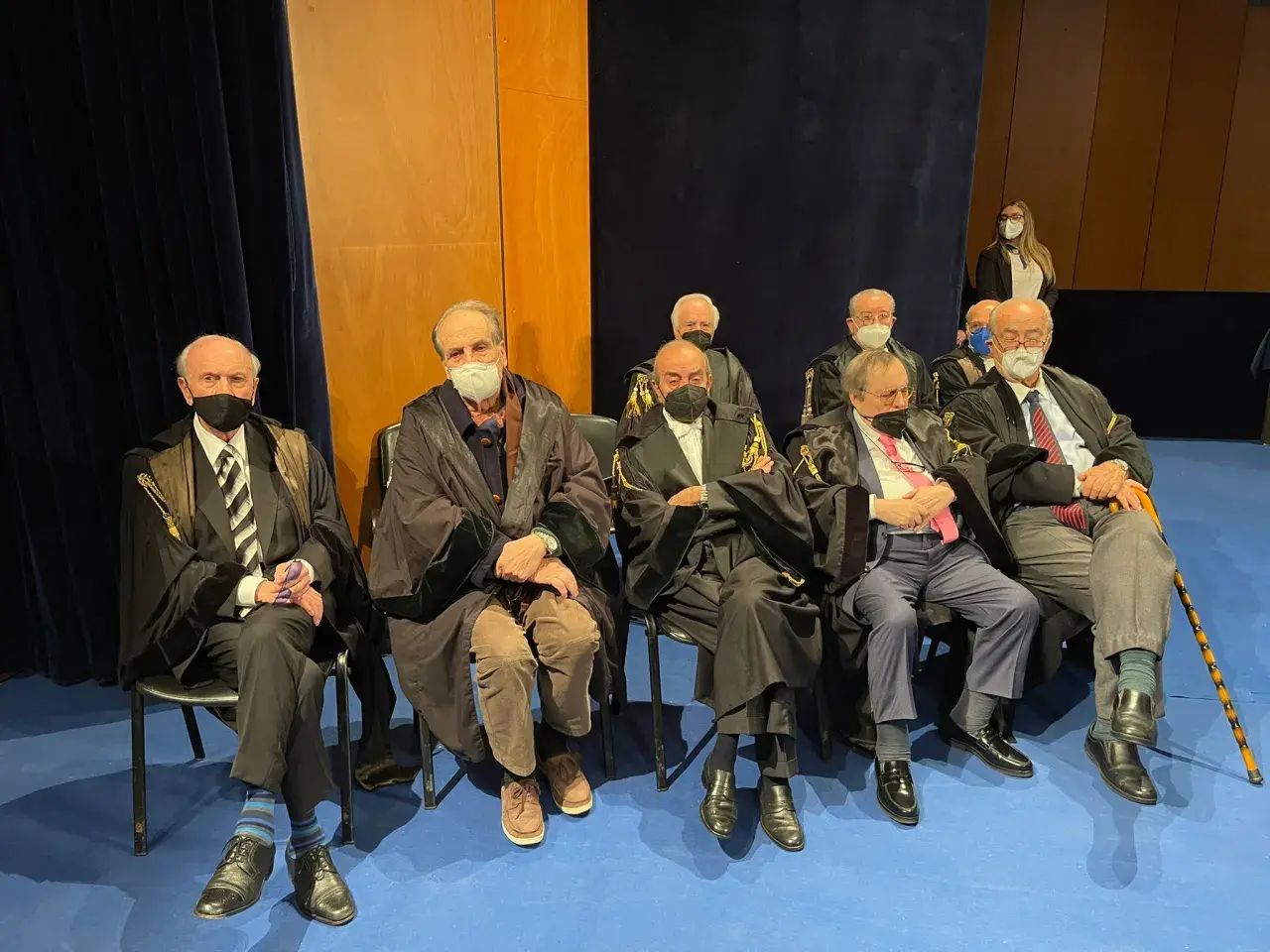 Uomini in toga seduti, alcuni con mascherina. Un uomo anziano potrebbe diventare avvocato a 50 anni, dimostrando che non è mai troppo tardi.
