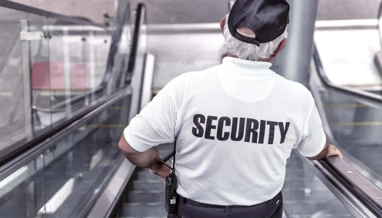 Un buttafuori con la scritta "SECURITY" sulla schiena, su una scala mobile. Chissà quanto guadagna un buttafuori per questo lavoro.