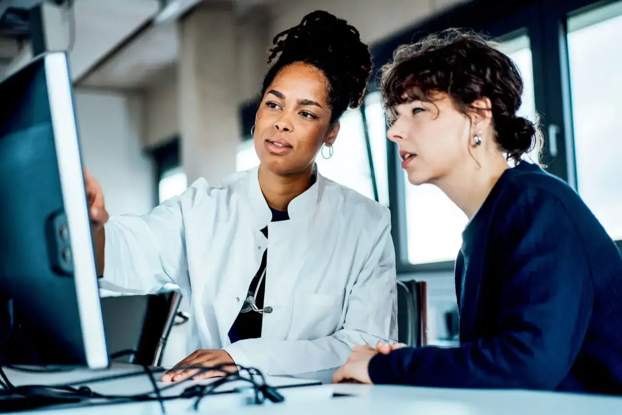 Due medici discutono al computer, forse analizzando dati su quanto guadagna un medico di base.