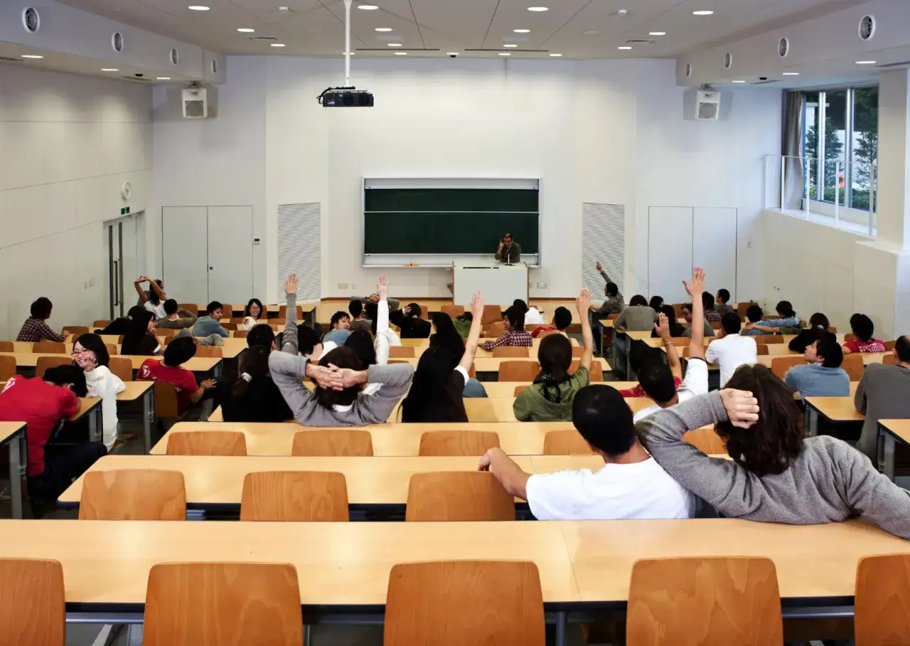 Aula universitaria con studenti che alzano la mano. Un'opportunità di università gratuita dopo i 50 anni, per imparare sempre.