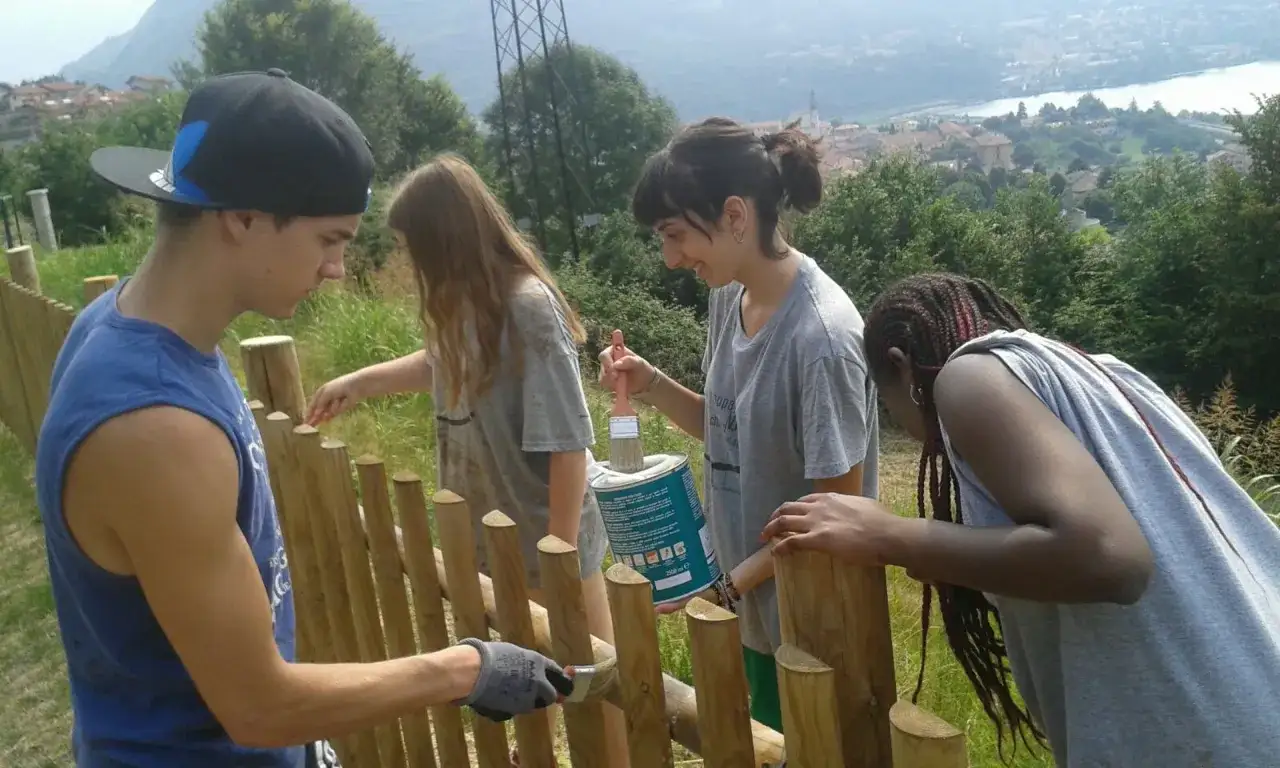 Ragazzi di 16 anni impegnati in lavori estivi, dipingono una staccionata in legno con vista panoramica.