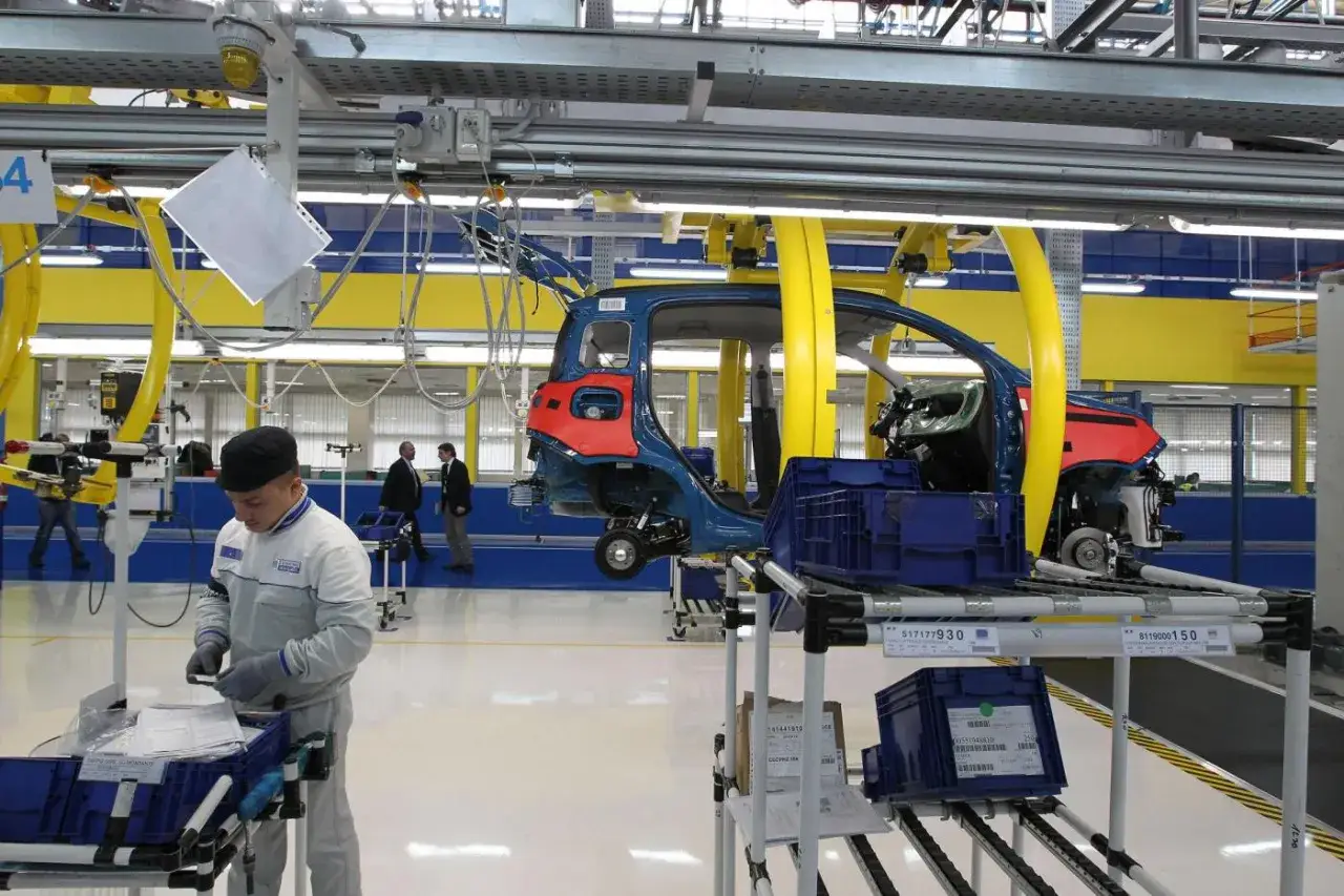 Un operaio di produzione lavora in una fabbrica automobilistica, con il telaio di un'auto sospeso sopra di lui.