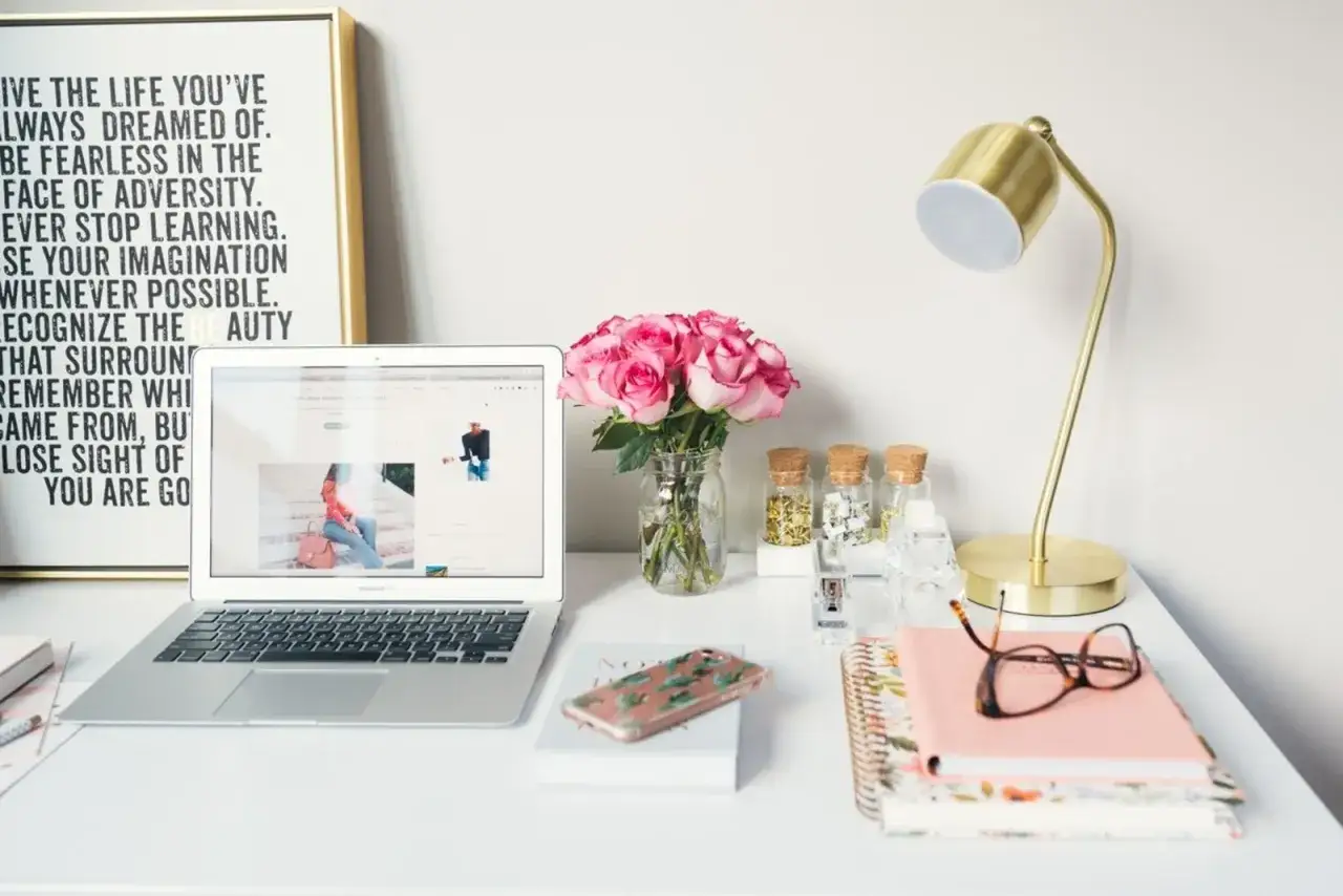 Scrivania ordinata con laptop aperto, fiori rosa e lampada dorata, perfetta per chi cerca lavori online per studenti.