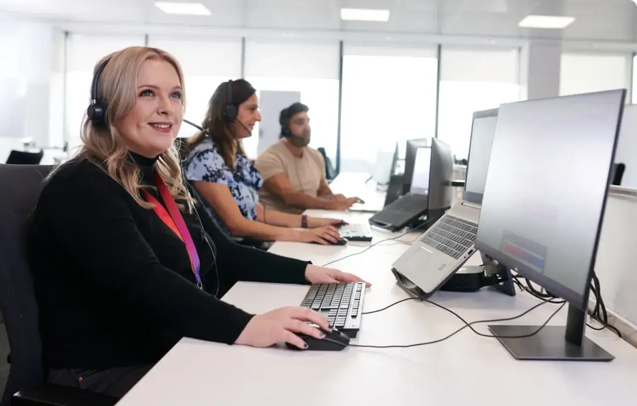 Operatori sorridenti con cuffie offrono assistenza clienti al computer, lavorando in un ufficio luminoso.