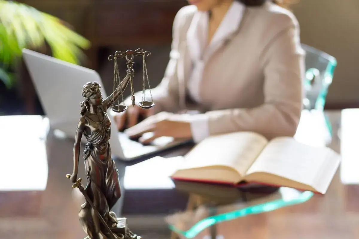 Statua della Giustizia, bilancia e libro aperto su una scrivania. Si indaga quanto guadagna un avvocato civile.