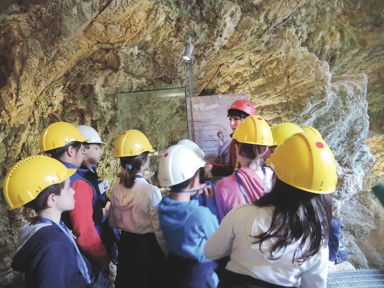 Bambini con caschi gialli ascoltano una guida in una grotta. Un geologo cosa studia? La storia della Terra, le rocce e i fossili.