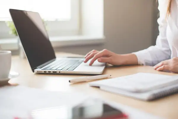 Mano su tastiera laptop, tazza caffè, quaderno. Ricerca su quanto guadagna un interprete per capire il potenziale di carriera.