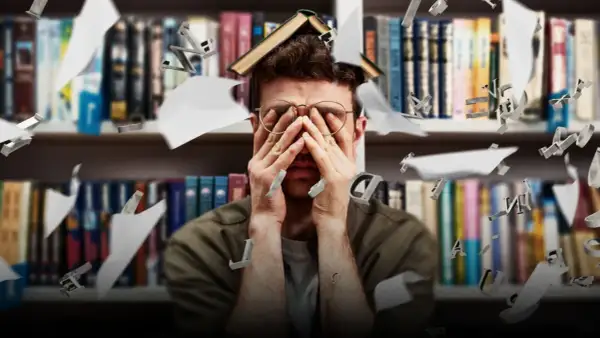 Studente sopraffatto tra libri e lettere volanti, riflette le sfide dell'università e degli sbocchi lavorativi.