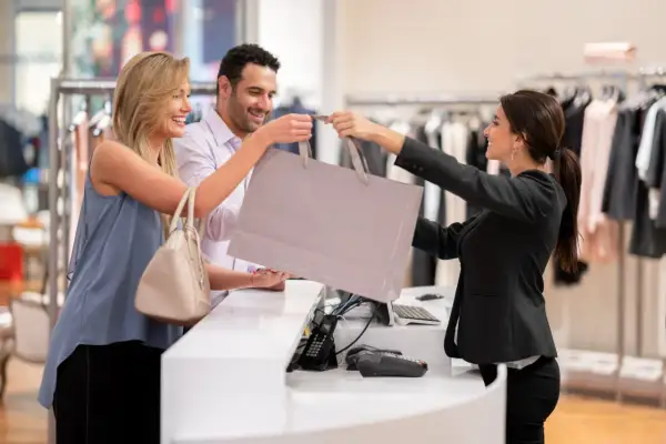 Una commessa sorridente consegna una borsa della spesa a una coppia felice in un negozio di abbigliamento.