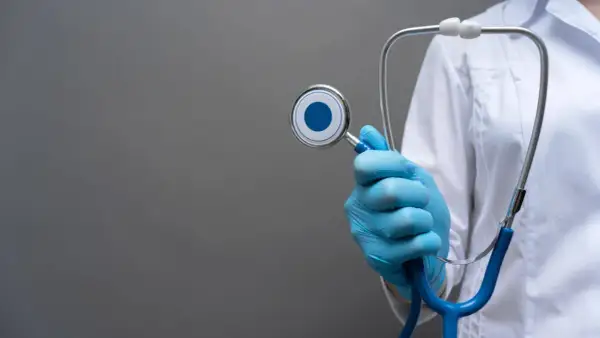 Mano con guanto blu tiene uno stetoscopio, simbolo del piano di studi medicina San Raffaele.