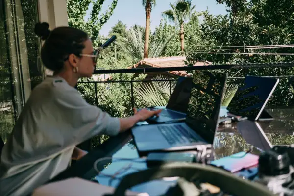 Donna lavora da remoto part time su un balcone lussureggiante, con laptop e tablet.