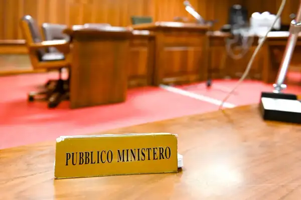 Targhetta "Pubblico Ministero" su un tavolo in un'aula di tribunale. Chi è il pubblico ministero? È colui che rappresenta l'accusa.