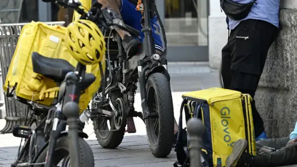 Corrieri Glovo con borse gialle e biciclette elettriche, pronti a lavorare.