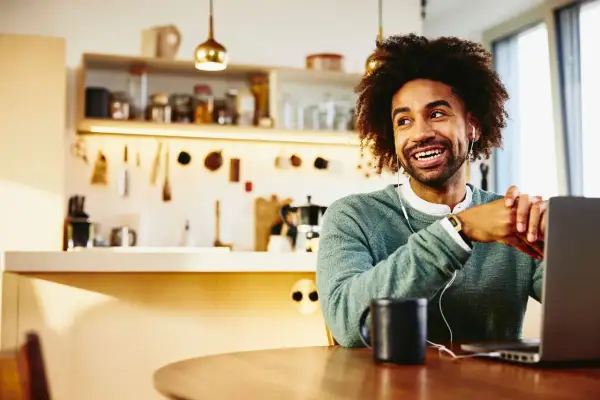 Uomo sorridente con cuffie lavora da casa al suo laptop, godendosi la flessibilità dei **work from home jobs**.