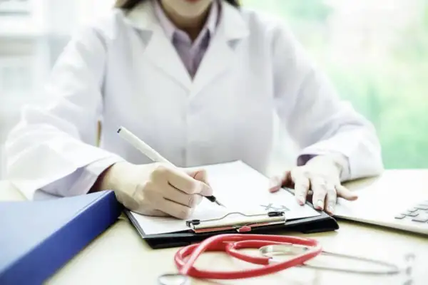 Medico legale che scrive su una cartella clinica, con stetoscopio e laptop. Quanto guadagna un medico legale?