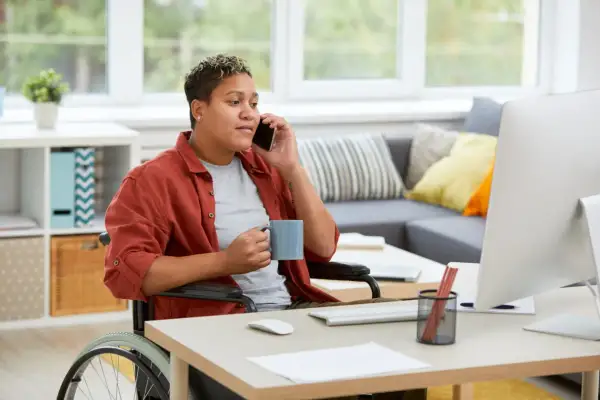Persona in carrozzina al telefono, con tazza in mano, lavora da casa. Un esempio di inclusione per le categorie protette.