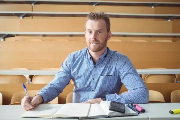 Uomo con barba rossa studia in aula, appunti e calcolatrice sul tavolo. Cosa studiare a 30 anni per trovare lavoro?