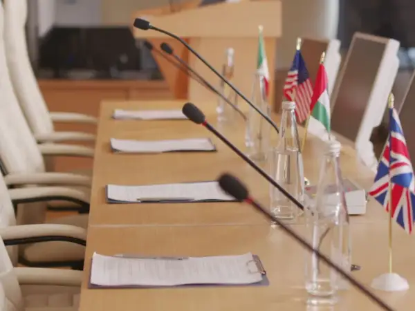 Tavolo da conferenza con microfoni, bandiere di diverse nazioni e fogli. Forse qui si discute come si diventa console.