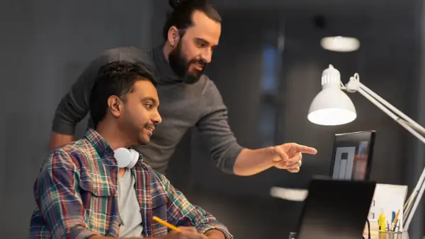 Due colleghi discutono un progetto al computer. Uno indica lo schermo, l'altro ascolta. Forse stanno valutando il project manager stipendio netto.