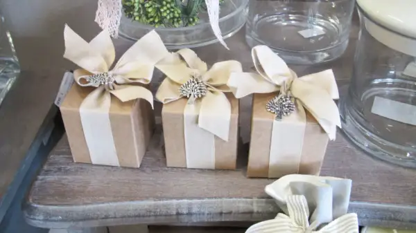 Piccoli pacchetti regalo marroni con fiocchi beige e ciondoli ad albero, perfetti per chi ama lavorare da casa confezionando oggetti.