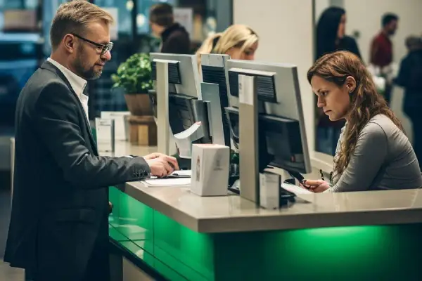 Uomo in giacca e donna al bancone di una banca, concentrati sul lavoro. Per lavorare in banca serve la laurea, e loro sembrano averla.