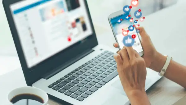 Gestione social media: un lavoro che può portare a un ottimo stipendio. La persona interagisce con notifiche e like su uno smartphone, accanto a un laptop aperto.