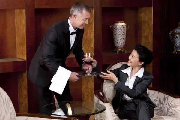 Maggiordomo in livrea serve un bicchiere di vino a una donna in un salotto di lusso. Chissà quanto guadagna un maggiordomo per un servizio così impeccabile.