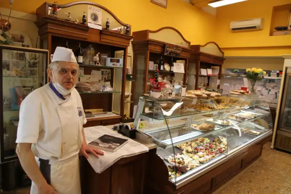 Pasticcere esperto, con vitto e alloggio, mostra la sua vetrina piena di dolci.