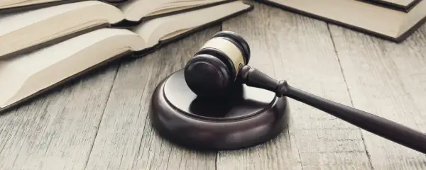 Martelletto da giudice su tavola di legno, con libri aperti sullo sfondo. Simbolo di giustizia e di studi di scienze giuridiche Pegaso.