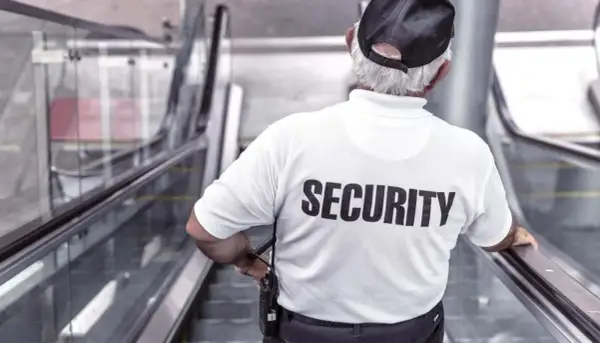 Un buttafuori con la scritta "SECURITY" sulla schiena, su una scala mobile. Chissà quanto guadagna un buttafuori per questo lavoro.