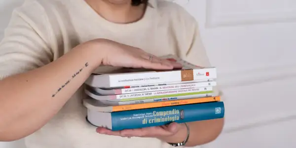 Mani che sorreggono libri, tra cui un "Compendio di criminologia". Quanti anni sono passati da quando si è iniziato a studiare il crimine?