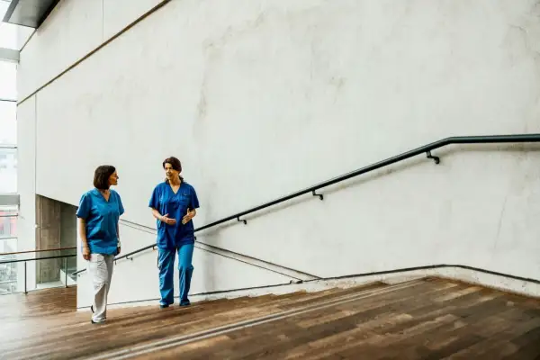 Due fisioterapiste in camice blu discutono sulle scale, forse valutando nuove offerte lavoro fisioterapista.